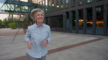 Kafkas kıdemli mutlu kadın sabah işe koşuyor dışarıda koşuyor olgun kadın CEO gülümsüyor yaşlı iş kadını aktivitesi acilen ofis binasına geç kalıyorum iş toplantısına geç kalıyorum