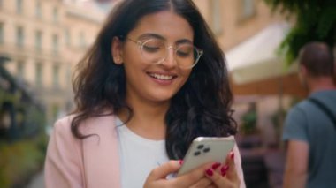 Mutlu bir şekilde gülümseyen Hintli Arap etnik kadın iş kadını gezgin kız cep telefonu uygulaması kullanarak şehir dışında internet üzerinden oyun alışverişi yaparak eğleniyor.