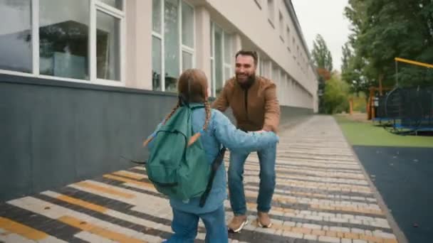 父亲从学校问候女儿喜欢小女生奔向爸爸拥抱接孩子回家快乐的欧洲家庭户外支持关爱爱让学生相遇 — 图库视频影像