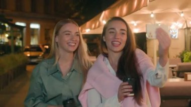 İki Avrupalı mutlu genç arkadaş görüntülü sohbet, cep telefonu, akıllı telefon, vlog turizm, selfie sokak kenti. Kameralı hafta sonu sosyal medyaya bakarak gülümseyen kızlar.