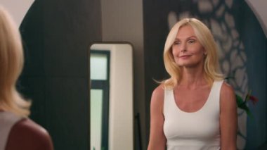 Güzel, beyaz, olgun, yaşlı bir kadın banyoya mutlu, orta yaşlı bir kadın gelir. Makyaj stili güzelliğini ayna yansımasında kontrol eder. Günlük cilt bakımı, yaşlanmayı önleyen doğal kozmetik ürünler.