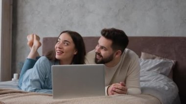 Birkaç mutlu ev sahibi beyaz kadın ve erkek yatak odasında rahat bir yatakta dizüstü bilgisayarla alışveriş yapıyorlar. İnternet 'ten alışveriş biletleri alıyorlar.
