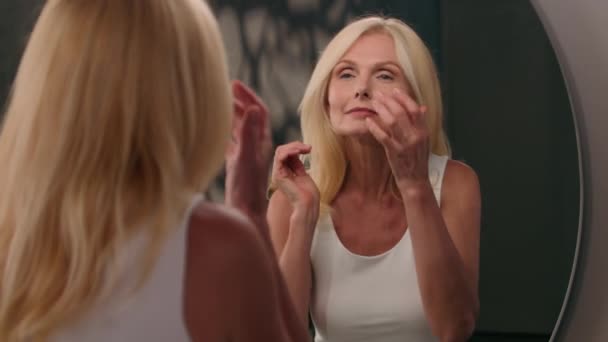 美丽的中年白种女人在浴室里成熟的老太太看着镜子里的自然美化妆品抗老化皱纹的面部护肤信息在手机上准备约会 — 图库视频影像
