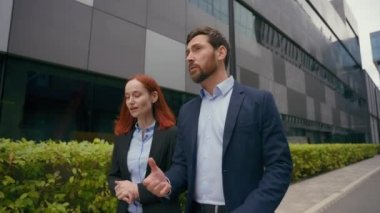 İki ortak iş arkadaşı şehirde yürür şirket anlaşması hakkında konuşur iş birliği yapar şehir merkezinde şehir dışında iş birliği yapar erkek ve kadın yöneticiler konuşur.