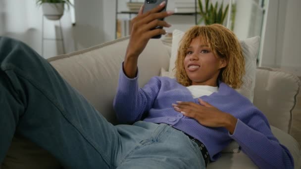 アフリカ系アメリカ人女性エスニックガールインフルエンサーストーリー ソーシャルメディアブログ 家でソファーソファに横たわる携帯電話でオンライン遠隔ビデオ通話 スマートフォン会話チャット — ストック動画