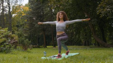 Sportif kıvırcık beyaz kadın, ince yoga eğitmeni spor antrenmanı yoga antrenmanı. Virabhadrasana savaşçısı pozu. Bir numaralı eğitim dengesi pozisyonu.