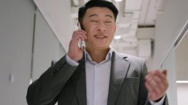 Mutlu Asyalı iş adamı Çinli Japon asıllı adam modern ofis koridorunda cep telefonunu arıyor. Neşeli iş adamı. Akıllı telefon görüşmelerine cevap ver.