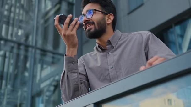 在城市阳台上微笑着的阿拉伯商人雇主在户外写字楼里用电话录音记录语音留言在城市里移动话筒扬声器中的语音信箱 — 图库视频影像