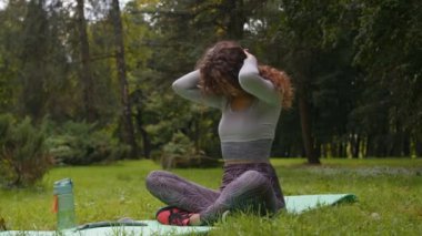 Parkta açık havada sportif, zayıf bir kadın boyun kaslarını gevşetiyor, başını eğip ısınıyor spor salonunda yoga antrenmanı yapan kızı eğitmeden önce ısınıyor.
