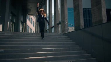 Kafkasyalı mutlu, kaygısız kadın şehirde dans ediyor neşeli iş kadını kız dans ediyor açık havada iş yerinin merdivenlerinden iniyor başarıyı telefonla müzik eşliğinde kutluyor.