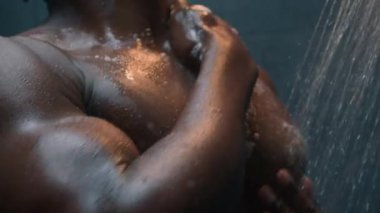 Afro-Amerikalı çıplak, seksi, çıplak, ıslak adam duş jeli sürüyor, sıvı sabun köpüğü köpük banyosu yapıyor, temiz cilt temizliği, erkek güzellik banyosu reklamı yapıyor.