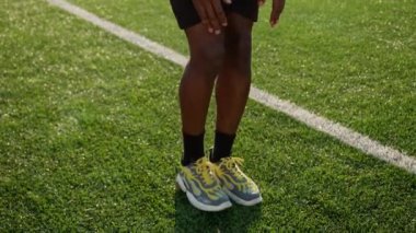 Güçlü fitness oyuncusu Afrika kökenli Amerikalı sporcu futbol sahasında güneş ışığı üzerine çömelme egzersizi yapıyor. Atletik erkek bir bacağının üzerinde ileri atlıyor. Spor, kalçaları çalıştırıyor.