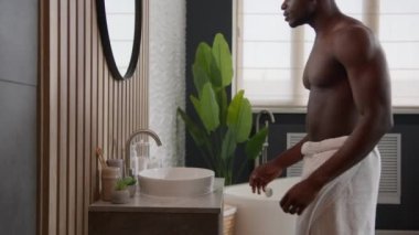 Afro-Amerikan erkek çıplak kaslı erkek yüzünü yıkıyor soğuk sıcak su banyosu yapıyor yüz bakımını temizliyor sabah hijyen tazeleyici nemlendirici anti-akne cilt bakımını evde yapıyor.