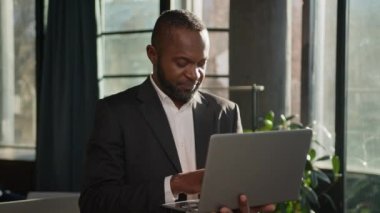 Kıdemli uzman 50 'lerin iş adamı dizüstü bilgisayarı güneş ışınlarında duruyor. Orta yaşlı, Afro-Amerikan erkek işveren çevrimiçi bilgisayar veri analizi yapıyor. Yetişkin iş adamı kameraya bakıp gülümsüyor.