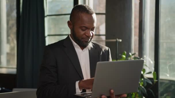シニアスペシャリスト50Sビジネスマンは サンビームオフィスのラップトップと立っています 中年アフリカ系アメリカ人の男性雇用主 オンラインコンピュータデータ分析 カメラ幸せな笑顔を見ている大人のビジネスマン — ストック動画
