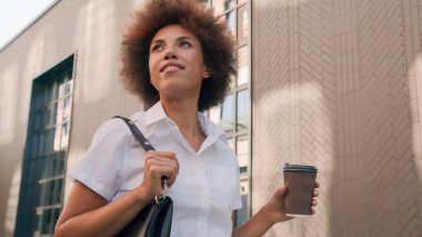 Elinde kahve fincanı olan mutlu Afro-Amerikan iş kadını şehir iş dünyasından çekici bir kızı alıp götürdü. Güzel bir bayan açık havada geziyor.