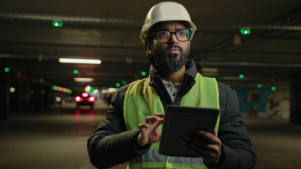 Форман осматривает парковку подземного городского промышленного инженера тяжелой промышленности арабского человека индийского строителя в каскадной шляпе архитектора производства рабочих цифровой планшет говорить видео-конференции
