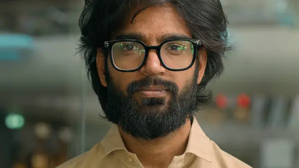 Portrait bearded Indian business man executive in office. Close up eastern male professional teacher businessman ethnic entrepreneur HR manager in eyeglasses posing indoors look down looking at camera