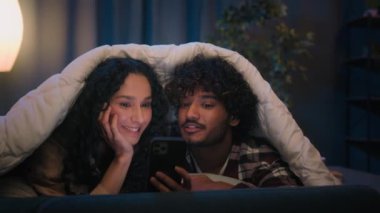 Gadget bağımlısı çok ırklı çift ve çeşitli kadın cep telefonlarını battaniyeli sosyal medya bağımlılığı altında birlikte kaydırıyorlar. İnternet alışverişinde inanılmaz indirim yapıyorlar. İyi haberler hayret verici.