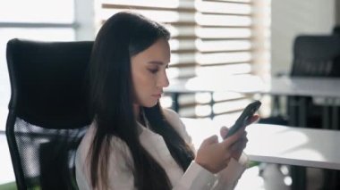 Ciddi iş kadını ofisteki telefonlarını karıştırıyor Kafkasyalı sakin kız sıkıcı iş kadını cep telefonu modern akıllı telefon uygulaması ağını kullanarak sosyal medya çalışanlarıyla sohbet ediyor.