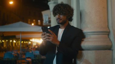 Genç, başarılı Hintli, Arap, akıllı cep telefonu kullanan, cep telefonu kullanan, açık havada mesajlaşan, gülümseyen, komik şans getiren, mutlu, mutlu, iyi haber veren, neşeli erkek.
