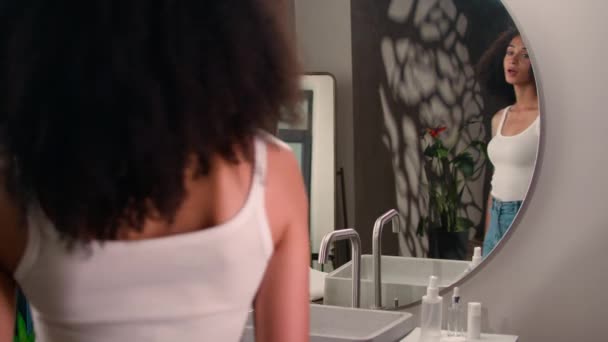 非洲裔美国女人来到家里的浴室 看着镜子里的倒影 美丽的少数民族姑娘 女士在整理卷发 做发型美发 日常洗发水走了 — 图库视频影像