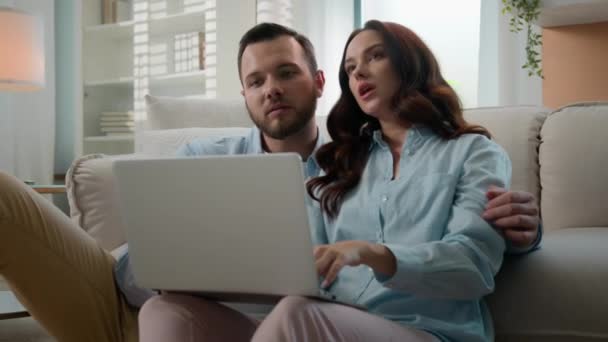 ラップトップのオンラインショッピングを持つコーカサスカップルの家族の男女は 電子商取引を一緒に検索して自分自身の新しいアパートを修理するための購入を指摘する家のための家具製品を選択します — ストック動画