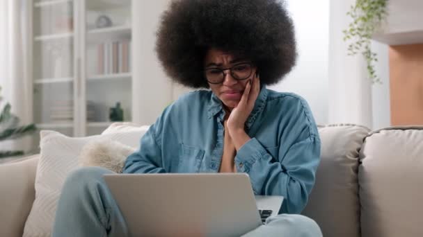 困惑愁眉苦脸的非洲裔美国女人在家里的笔记本电脑里读着可怕的坏消息沙发上的女用户自由职业者女商人用电脑休克压力伤心心烦意乱害怕上网问题麻烦 — 图库视频影像