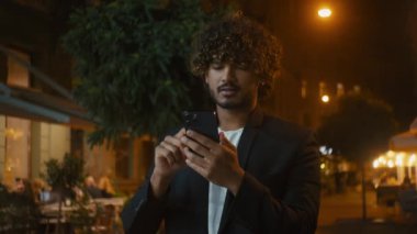 Genç Hintli Arap Latin Amerikalı adam akıllı cep telefonu kullanıyor. İnternet üzerinden mesajlaşıyor. Açık havada sohbet ediyor.