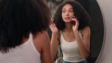 Mutlu Afrikalı kız cep telefonuyla gülen, konuşan, akıllı telefon konuşan, hoş sohbet banyodaki aynaya bakan, saç kesimini kontrol eden, saç stili gülüşü yapan, dedikoducu.
