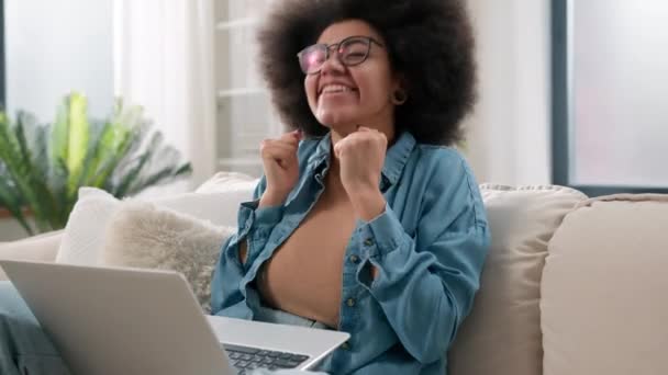 アフリカ系アメリカ人少女学生フリーランサー女性バイヤークライアントホームリビングルームスクリームソーシャルメディア良いニュースビジネス成功女性の達成ラップトップコンピュータ勝利賭けカジノ — ストック動画