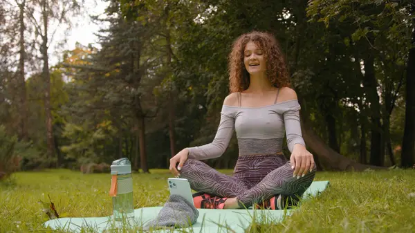 Beyaz kadın etkeni dışarıda parkta kayıt altında video blogunda video blogu çevrimiçi canlı yayın spor eğitmeni kız blogcu fitness yoga minderi üzerinde merhaba antrenör konferansı akışı