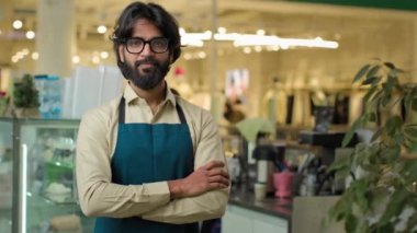 Mutlu, güler yüzlü kafe çalışanı, önlük kafeteryasında çalışan Hintli erkek garson. İşyerindeki küçük işletme servisinde çalışan Arap kahveci adama el işareti gibi el hareketi yapıyor.
