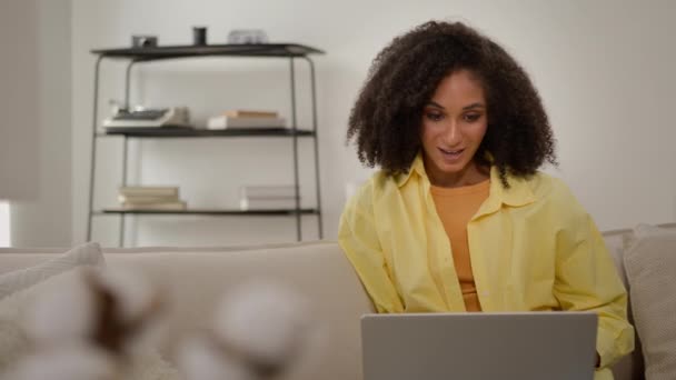 アフリカ系アメリカ人の少女フリーランサー 家からコンピュータを働かせて幸せな驚きの女性のビジネスマンはソファーのラップトップを使用して勝利の衝撃を喜びます 良いニュースは成功した達成を祝います — ストック動画
