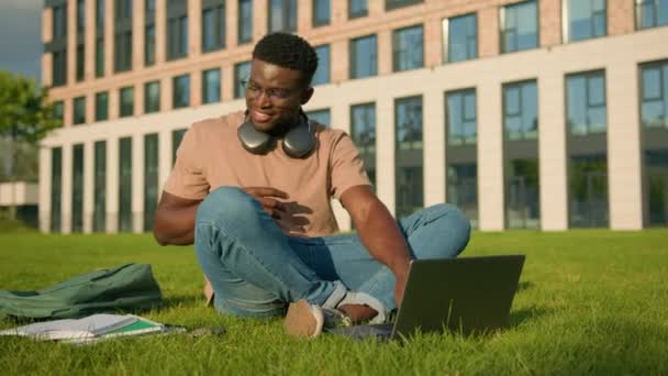 快乐微笑的非洲裔美国人美国大学学院男生男生在公园的草地上在线学习作业 用书本笔记本准备考试 — 图库视频影像