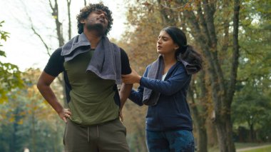 Arap acı çeken yorgun koşucu erkek bacak ağrısı çekiyor spor koşusu yapan Hintli kadın koşucunun koşuya yardım etmesinden sonra diz ağrısı acı çekiyor parkta koşan çifte kramp giriyor.