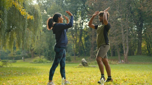 Indian Arabian couple outdoors together woman man in park sport guy girl friends athletes doing lunge training at nature high five gesture partnership friendship achieve teamwork support stretching