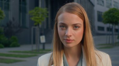 Ciddi derecede başarılı, kendine güvenen, beyaz, güzel, kadın, iş kadını, girişimci, profesyonel yönetici, iş yerinin yakınındaki kameraya bakan iş kadını, açık havada kadın portresi yapıyor.