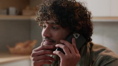 Evde telefonla konuşan mutlu Hintli adam internetten iş görüşmesi yapıyor. İspanyol adam akıllı telefon konuşuyor. Uzaktan iletişim kuruyor. Arap erkek mutfakta gülümseyen mobil konuşmalar yapıyor.
