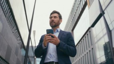 Beyaz tenli orta yaşlı pozitif işadamı, şehir erkek girişimci işadamı iş adamı sohbet ediyor, akıllı telefon ağı ile uzak iletişim bağlantısı kuruyor cep telefonuyla mesajları kaçırıyor.