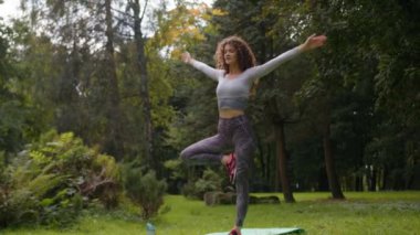 Beyaz tenli zayıf kas esnekliği Park 'ta bir bacağının üzerinde sakin spor kadın dengesi formda form tutan kız yogi iyi egzersiz yapan yoga yapan kadın ağaçta ayakta durup bacağını uzatıyor.