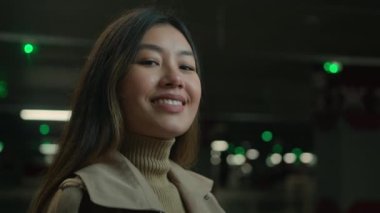 Asyalı, mutlu, etnik 20 'li yaşlarda, neşeli, güzel bir kız karanlık bir otoparkta kameraya bakıp gülüyor, Çinli, Japon bir bayan gülüyor, neşeli gülüyor, diş bakımı yapıyor.