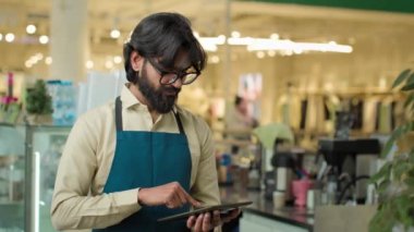 Kafe 'de çalışan Hintli erkek garson dijital tablet kafeterya çalışanı Arap barista satıcısı küçük işletmelere gülümseyen kablosuz bilgisayara menüyü not ediyor.