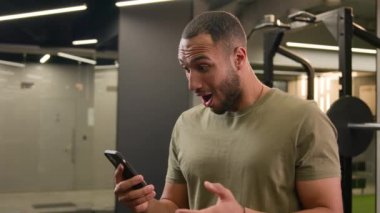 Komik, mutlu, kaygısız, Amerikalı Latin erkek sporcu formda, sporcu fitness eğitmeni, beden eğitimi sporcusu, cep telefonu başarısına şaşıran sporcu.