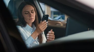 Beyaz kadın, bayan şoför, otoparkta arabasının içinde oturan, akıllı telefonları kurcalayan, cep telefonu stresi, kötü haber, mutsuz, endişe verici anksiyete sorunu.