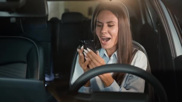 白人女性 ドライバー ビジネスマートフォン ブラウジング 駐車場で車の自動車の中に座っている 幸せなニュース オファー 勝利成功キス 携帯電話の画面 お祝い — ストック動画
