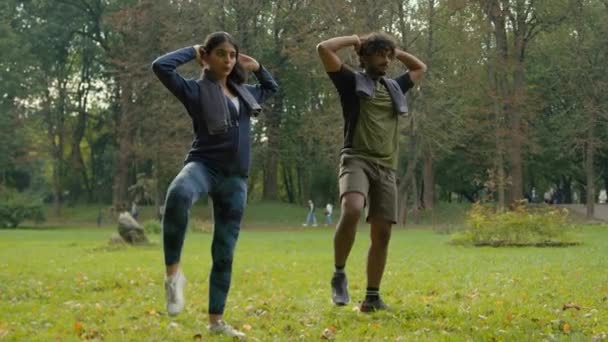 双语笑话 印度男子运动员教练个人健身教练阿拉伯女子女运动员适合在公园里一起做运动训练站在室外抬腿到肘部 — 图库视频影像