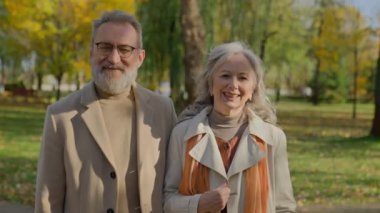 Sonbahar parkında gülümseyen olgun bir çiftin portresi. Neşeli, yaşlı bir adam. Doğada kameraya poz veriyor.