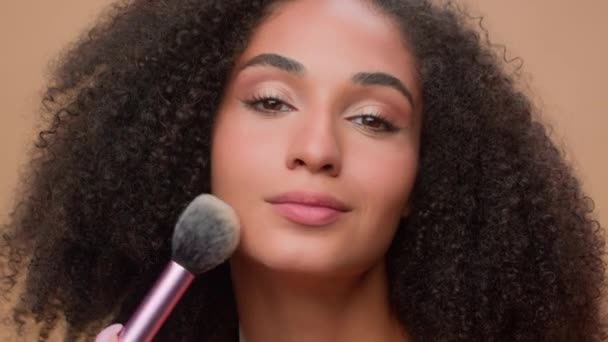 近景肖像米色画室背景美丽的非洲裔美国女人有着完美光滑的皮肤用粉末看着相机迷人的少数民族女孩粉末状化妆品脸红的美丽 — 图库视频影像