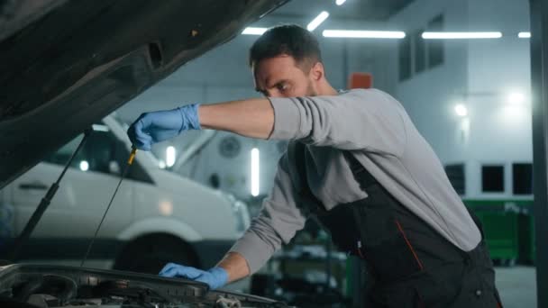 自動車修理工場で車のフードを開く30代男性 オートサービスでエンジンオイルレベルをチェック 男性メカニカルメンテナンスエンジニア ガレージで車を修理 ディップスティックツール 燃料車をチェック — ストック動画